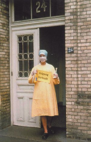 Sygeplejerske med isolationsdragt og podningsglas i hånden foran bygning med smitteudsatte på Blegdamshospitalet i september 1970